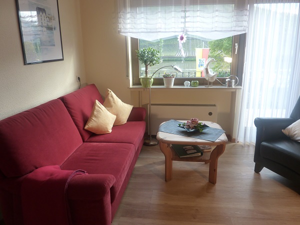Wohnraum der Ferienwohnung Mosel mit rotem Sofa am Fenster